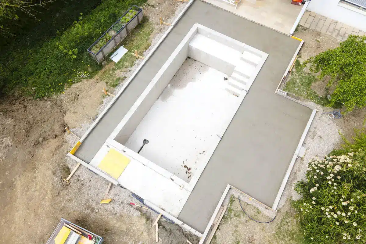 Construction piscine béton et aménagement terrasse Piscine en béton en construction avec terrasse coulée et escaliers intégrés dans un jardin.