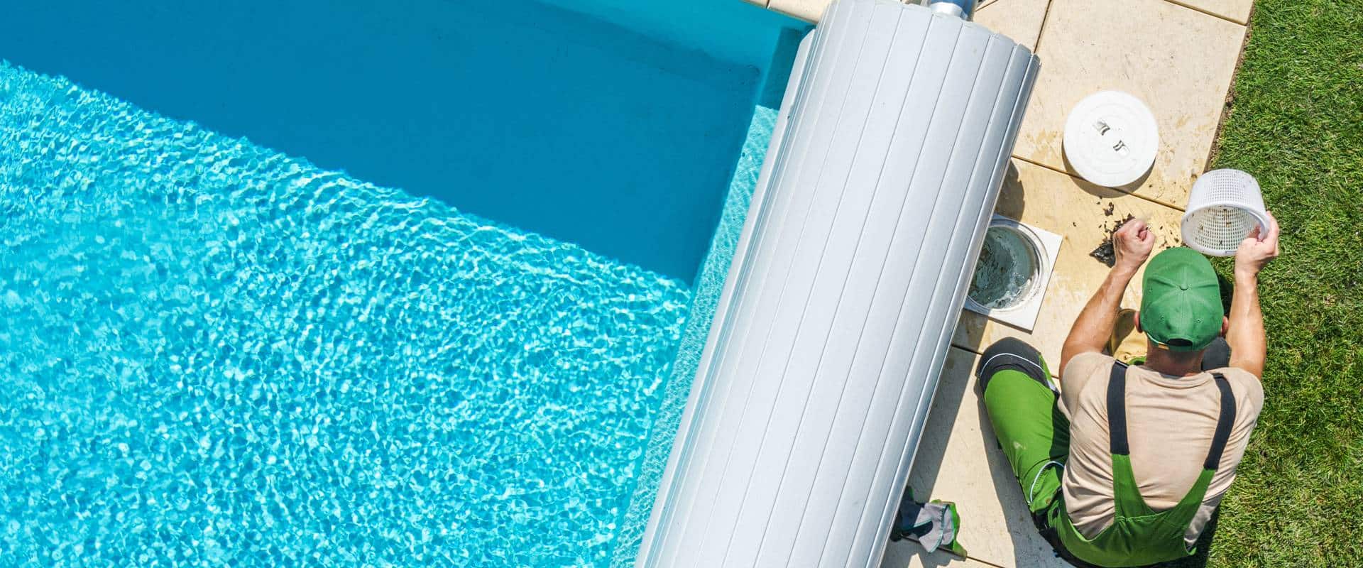 Technicien de piscine en vert nettoyant un panier de skimmer près d'une couverture automatique.