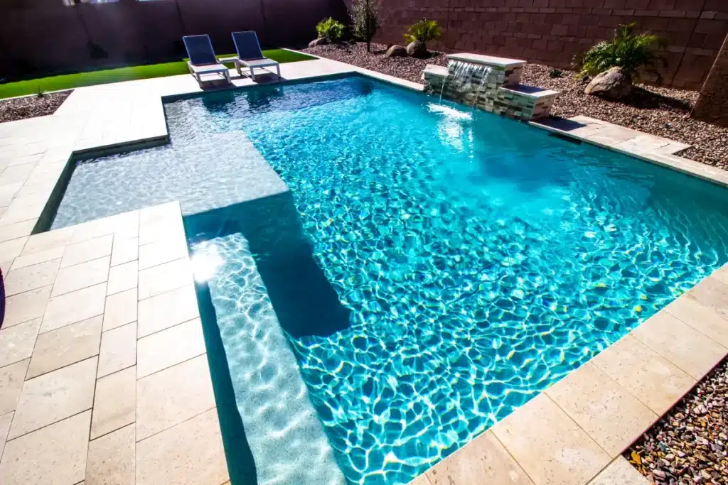 Aménagement Piscine Moderne : Cascade et Plage Immergée Piscine turquoise avec cascade et plage immergée sur terrasse dallée moderne dans un jardin paysager.