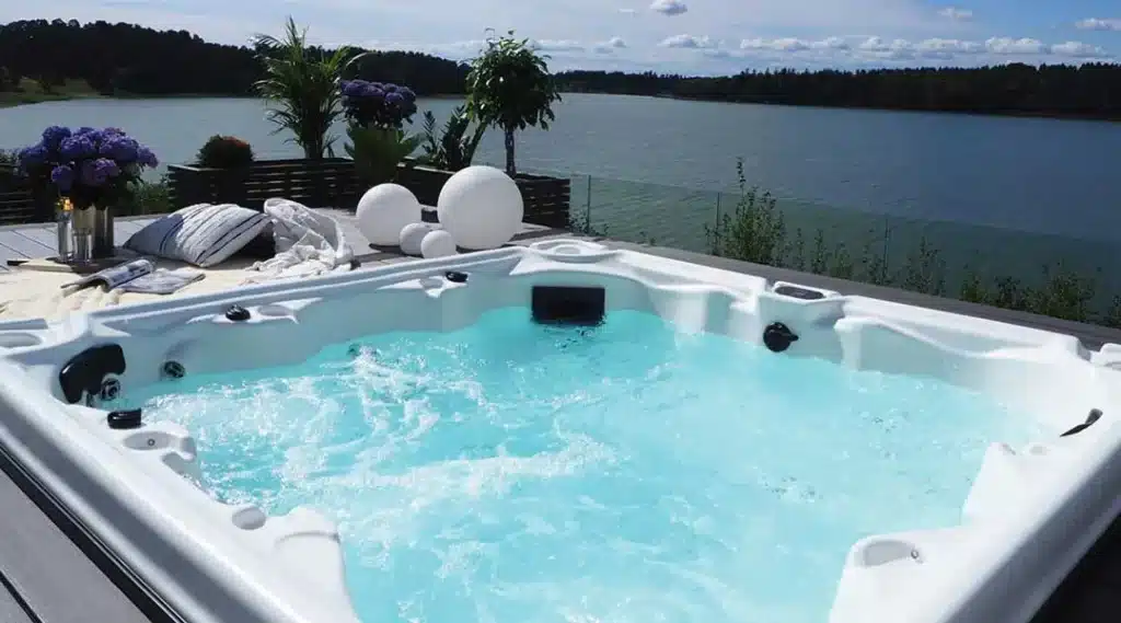 Détente en Spa Extérieur avec Vue Panoramique sur Lac Spa extérieur bouillonnant sur terrasse en bois avec vue lac, décoré de plantes et sphères blanches modernes.