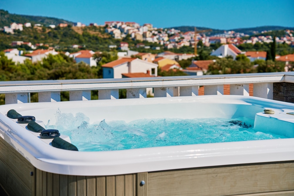 Jacuzzi avec vue panoramique sur une terrasse ensoleillée Jacuzzi bouillonnant sur une terrasse avec vue panoramique sur un village côtier et les collines.