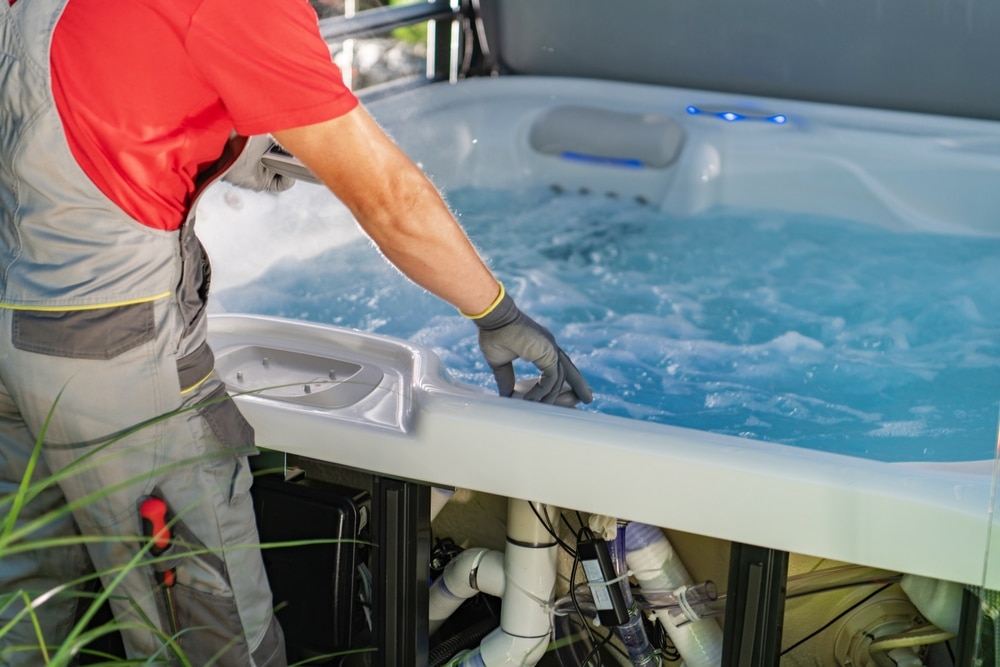Maintenance et réparation professionnelle de spa jacuzzi Technicien effectuant la maintenance d'un spa jacuzzi avec les composants internes visibles et eau bouillonnante.