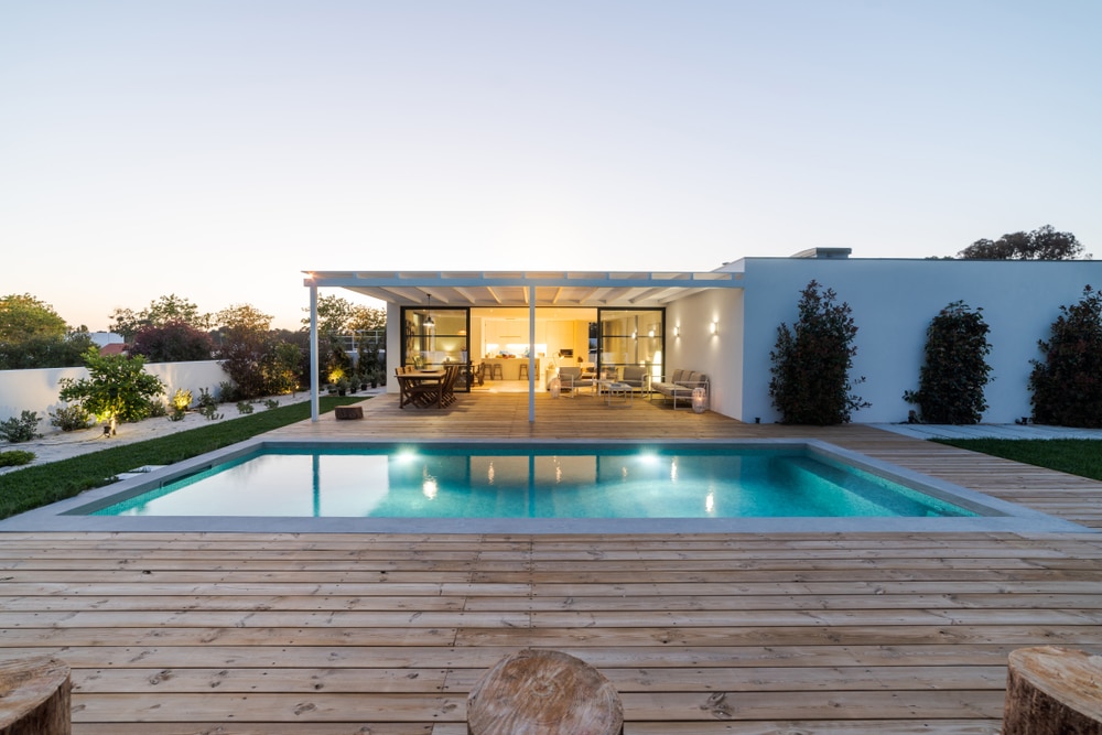 Maison moderne avec piscine et terrasse bois design Maison moderne avec piscine éclairée, vaste terrasse en bois et pergola au crépuscule. Design épuré et chaleureux.