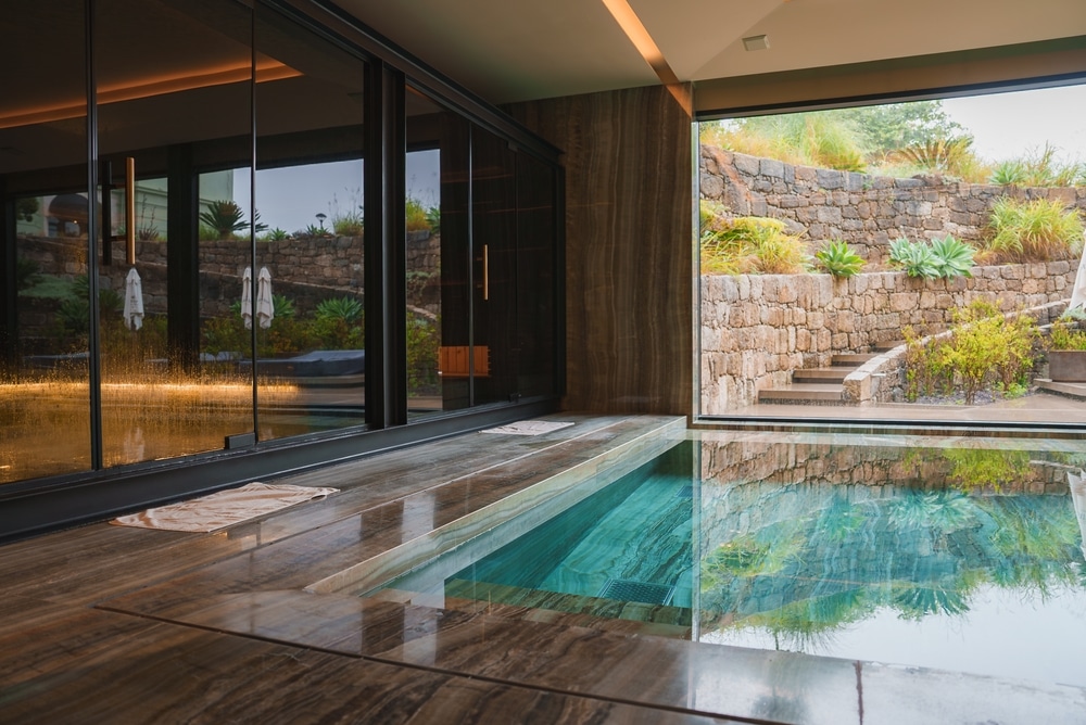 Spa de Luxe : Piscine Intérieure avec Vue sur Jardin Piscine intérieure spa de luxe avec sol en marbre et vue panoramique sur un jardin en terrasse fleuri.