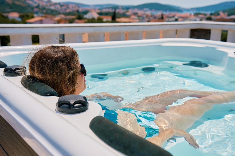 Relaxation en jacuzzi sur un toit avec vue mer panoramique Femme relaxant dans un spa extérieur sur un toit avec vue panoramique sur une ville côtière ensoleillée.